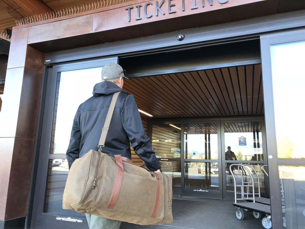 A man carries a Bellemonde Brown Faux Suede Gear Bag while walking into a building entrance with glass doors